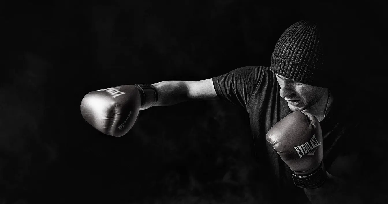 A boxer in black throws a punch out of the dark, eyes locked on the target.